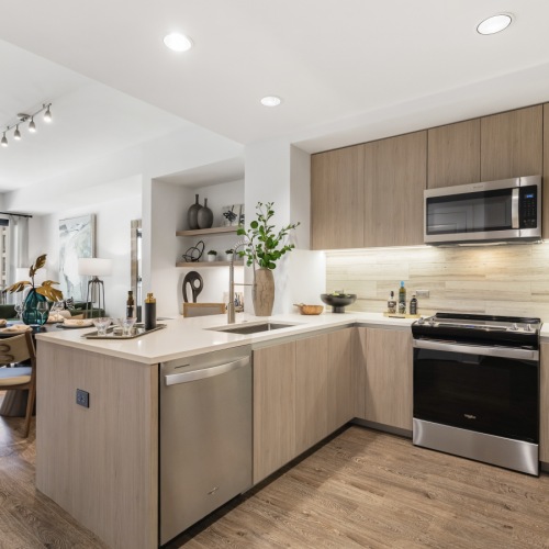 apartment kitchen with u-shaped counter, light flat wood cabinetry, stainless steel appliances, and white stone counters apartment kitchen with u-shaped counter, light flat wood cabinetry, stainless steel appliances, and white stone counters